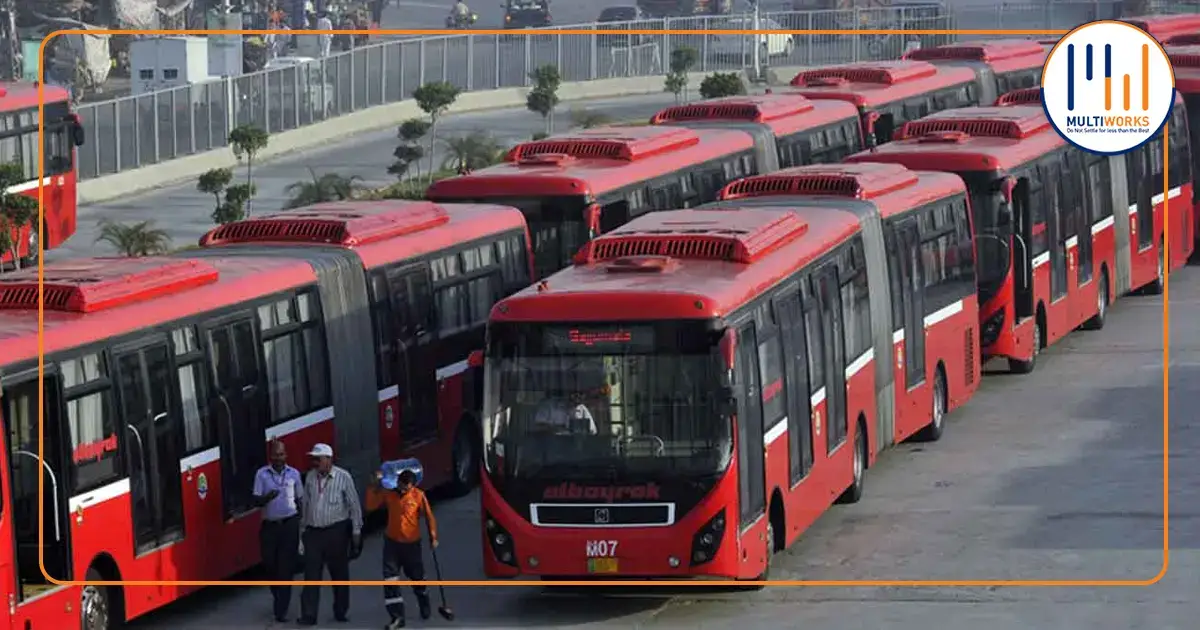 Red metro buses parked in a terminal with workers inspecting, highlighting Punjab government's metro service extension in Pakistan.
